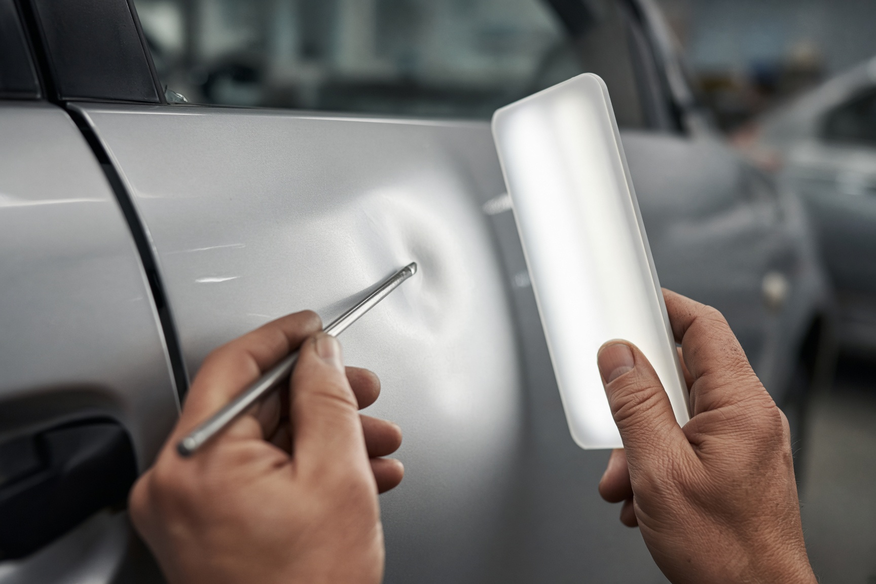 Technician working a dent out of a silver car door